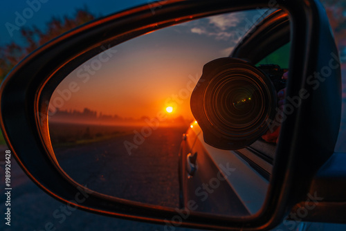 Camera lens reflected in car mirror at sunset, photography travel concept