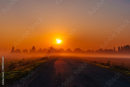 Empty road leading into sunrise with fog and warm light