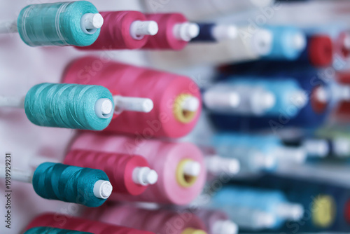 Photos Side view of many colorful sewing thread spools on a vertical wall holder in a w