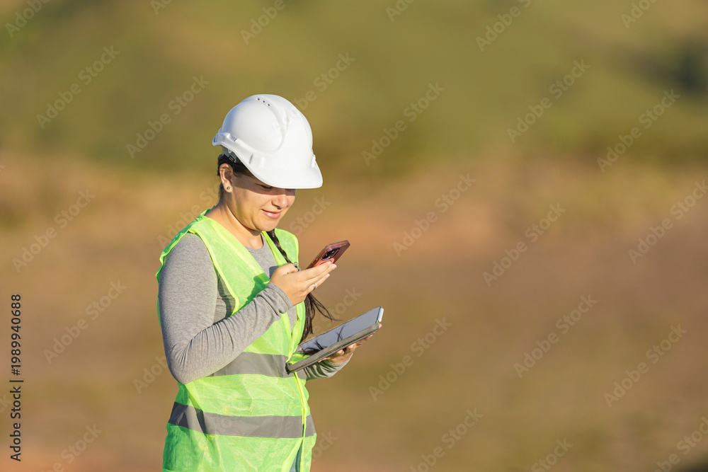 Fototapeta premium Woman construction engineer checking data on smartphone and tablet