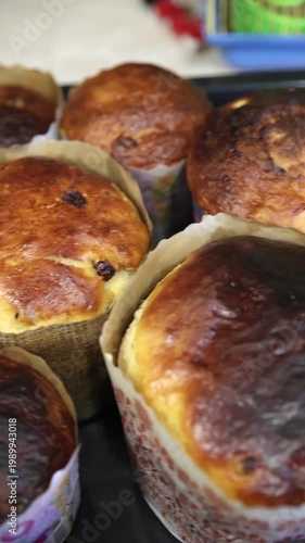 Detailed close-up of a freshly baked traditional Easter kulich paska with a glossy golden-brown crust and visible raisins. Baked in a paper form, showing beautiful texture and homemade quality. 