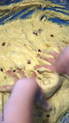 Close-up view of small children hands deeply immersed in thick, sticky yellow dough with raisins inside a bright blue bowl. Messy and joyful sensory baking moment, perfect for family cooking and kids 