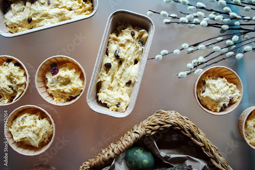Raw dough with raisins for cooking easter cakes in molds, pussy willow twigs, colored eggs in the basket 
