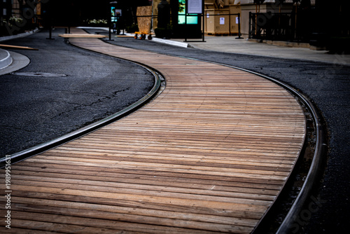 Curving wooden boardwalk alongside a dark asphalt path with metal edging