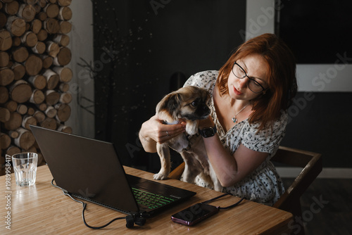 Concerned woman holding her puppy during an online video consultation with a veterinarian on a laptop. Telemedicine for pets, remote vet care, and animal health concept.