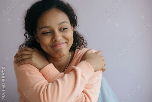 Girl smiling while hugging herself in a room with soft colors and natural light during daytime