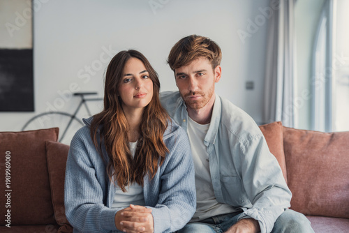 Schilderij op canvas Young couple sitting together on a couch in a modern home looking relaxed and th