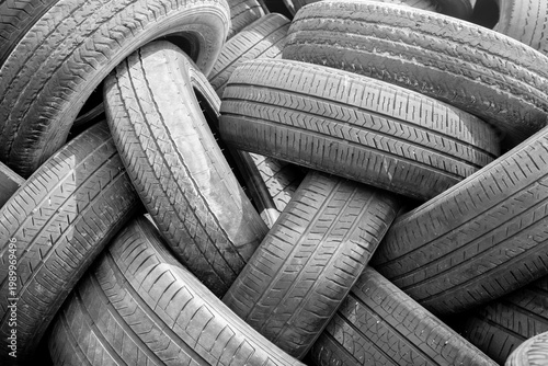 Black and white close-up of a pile of used car tires stacked chaotically. Abstract background with detailed tread pattern texture. Automotive, recycling and waste concept.