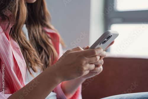 Canvastavla A young woman sits on a sofa using her smartphone, focused on typing and scrolling