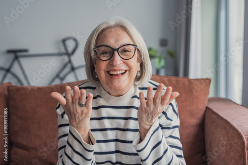 Cuadro en lienzo Smiling senior woman at home chatting and gesturing on a video call from her liv