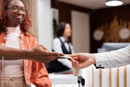 Canvastavla Young man giving money to steward at front desk counter in lobby, paying cash for services to carry trolley bags