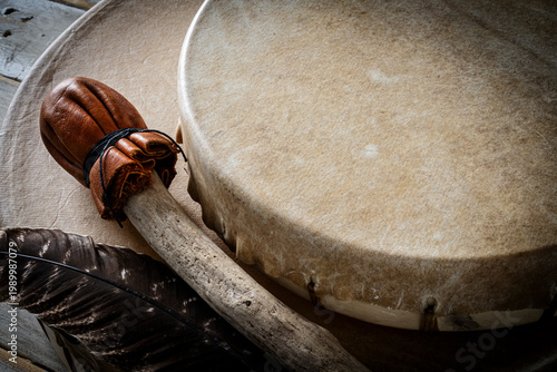 A low angle image of two handmade leather meditations drums with paddle and sacred feather. 