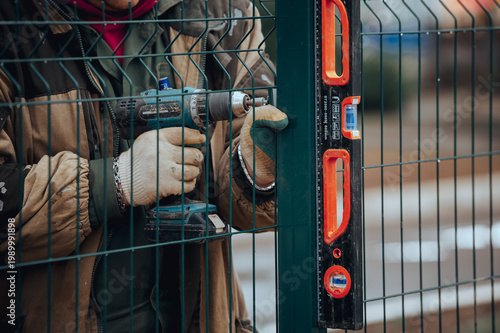Foto Worker installing metal fence using construction level tool