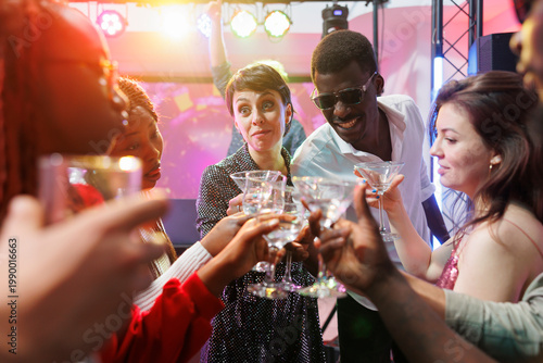 Foto Cheerful young clubbers clinking glasses with beverages, saying toast and celebrating