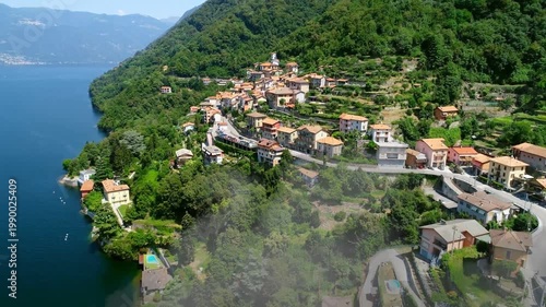 Drone approaching hillside village, mist drifting from lake, showing terraced roofs for tourism
