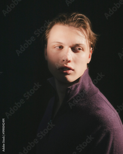 Blonde man in plum purple zip neck sweater gazes away left in wistful reflective three quarter profile moody sensitive studio editorial menswear portrait
