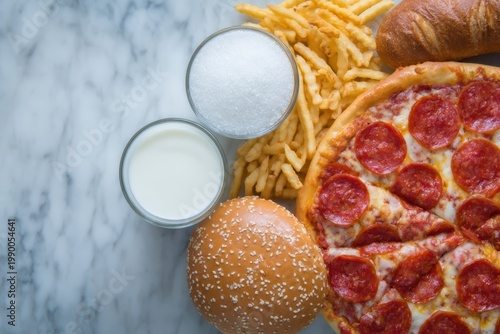 Unhealthy fast food assortment with sugar, milk, pizza, fries, and burger bun on marble surface