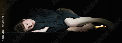 Obraz na płótnie The image portrays a figure curled up on a dark surface, exuding serenity and peace, highlighted by subtle lighting that emphasizes softer emotional states and vulnerability