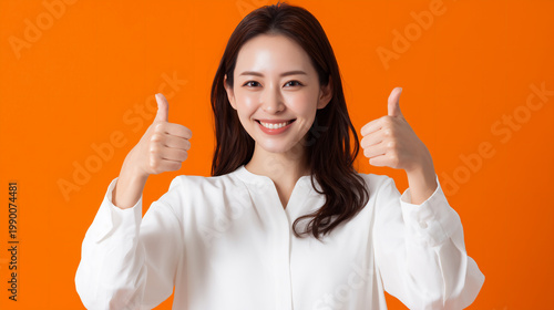 Happy Japanese businesswoman giving double thumbs up on orange background