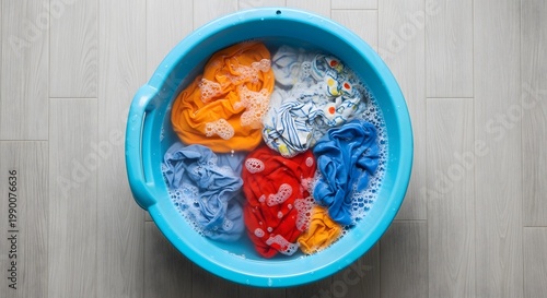 Overhead view of colorful garments soaking in a plastic basin filled with soapy water, ready for a wash cycle, domestic chore concept.