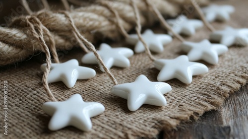 White ceramic star ornaments scattered on rustic burlap fabric with twine, creating a charming DIY holiday decoration scene. Perfect for crafting festive garlands or tree decorations.