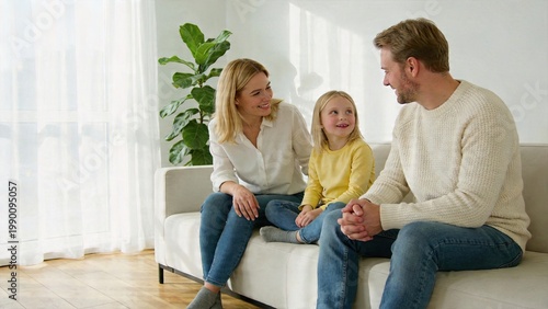 Happy Caucasian family mother father and daughter sitting on white sofa in living room bright home interior parent and child interaction conversation at home casual clothing