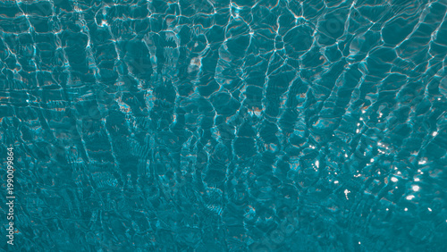 Sunlight reflecting through clear swimming pool water creating abstract caustic patterns on the blue floor. Abstract wallpaper, backdrop, background.