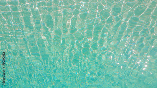 Fotografía Sunlight reflecting through clear swimming pool water creating abstract caustic patterns on the blue floor