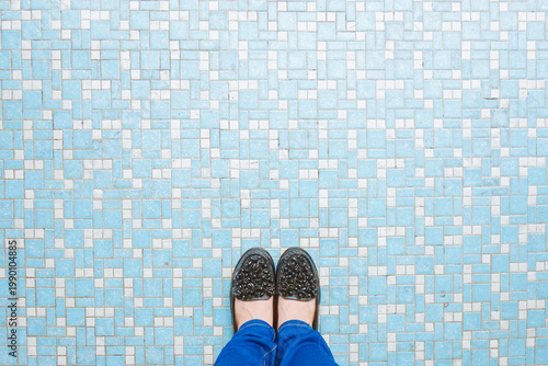 woman legs in blue jeans and in black shoes on mosaic tiles floor tile background