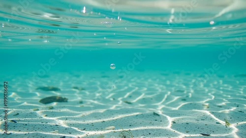 Underwater ocean surface with sunlit sandy seabed and rising bubbles