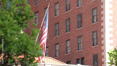 Droopy US Flag Hangs Near Old Building With Tree.