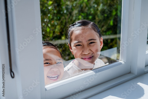Young Maori girls smiling while looking through the glass window outdoors on sunny day