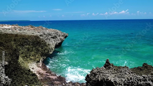 Natural Rock Arch Formation Over Turquoise Ocean with Crashing Waves and Island on Horizon - 4K footage