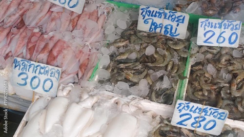 Seafood counter with fresh catch on ice with Thai language labels reading shrimp, squid and blue crab at street market