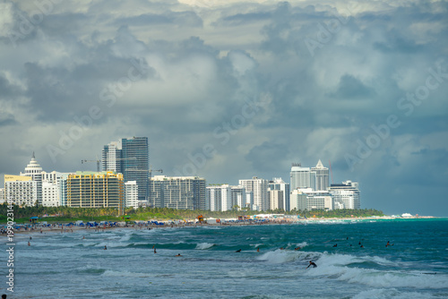 South Beach shoreline with hotels and surfers in ocean. Wide view of Miami South Beach with high-rise hotels, waves, surfers and heavy clouds in the sky.