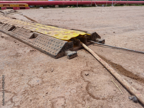 Photography ​Outdoor yellow and black heavy-duty rubber cable protector ramp on dirt ground,