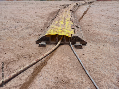 Fotografie ​Outdoor yellow and black heavy-duty rubber cable protector ramp on dirt ground,