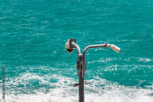 Security surveillance cameras on metal pole above turquoise sea with waves