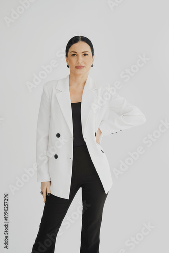 Woman stands confidently in a white blazer and black outfit in a bright room