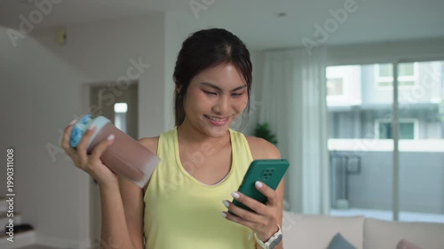 Young asian active woman drink whey creatine shake bottle eating diet food using phone calorie plan app after home sport workout. health care asia people happy relax protect aging life weight loss.