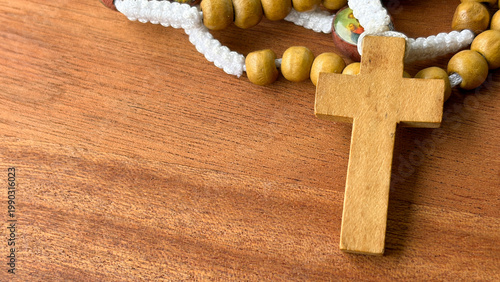 Minimal composition of wooden cross with rosary beads on wooden surface representing devotion spirituality and sacred reflection.