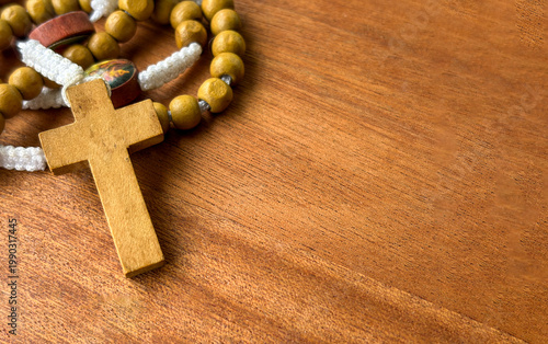 Wooden cross and rosary beads on wooden tabletop representing religious faith prayer tradition and inner peace.