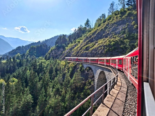 Red train on curved viaduct in the Swiss Alps near St. Moritz, scenic railway journey, Switzerland