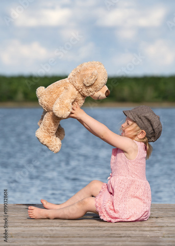 little girl sitting on the pier with her teddy