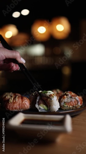 Vertical screen sushi roll dipped into soy sauce chopsticks close view slow motion fresh seafood japanese cuisine appetizing detail
