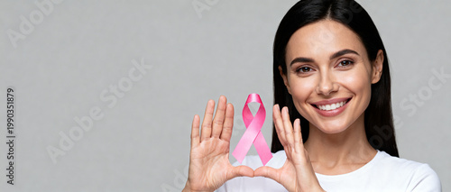 Smiling young woman happily holding a pink awareness ribbon perfect for supporting breast cancer survivors and charity