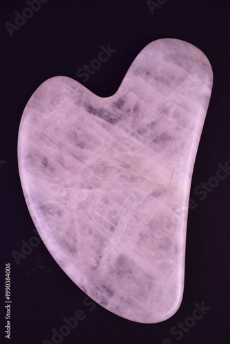 Gouache scraper for facial massage made of rose quartz on a black background. Close-up.
