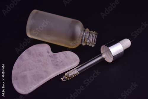Gouache scraper and serum for facial massage on a black background. Close-up.
