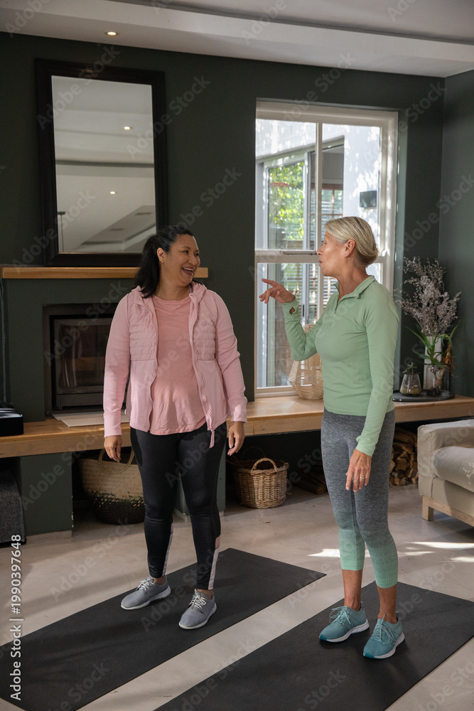 Obraz premium Senior female friends chatting on black yoga mats in living room beside fireplace wearing sneakers