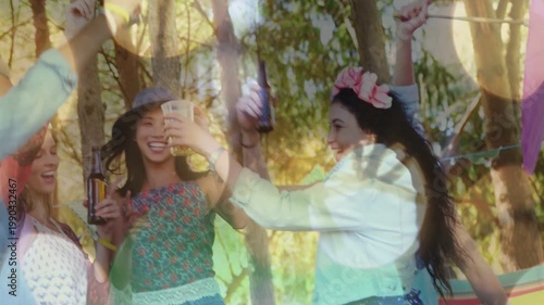 Diverse friends dancing and clinking bottles and plastic cups at campsite, wearing flower crowns